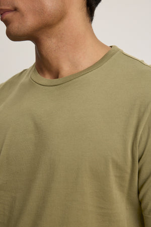 A close-up of a person wearing the HOWARD TEE by Velvet by Graham & Spencer in plain olive green Pima jersey, highlighting the neck, shoulder, and upper chest for a perfect fit.