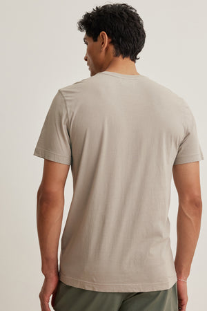 A person wears the HOWARD TEE by Velvet by Graham & Spencer, a light gray t-shirt made of lightweight Pima jersey, and green pants. Facing away against a plain background, they showcase a perfect fit with vintage charm.