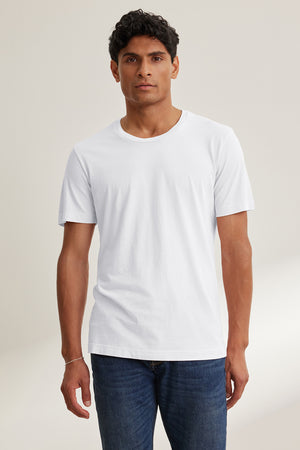 Wearing the HOWARD TEE by Velvet by Graham & Spencer, a person in dark jeans stands against a neutral background, showcasing an effortlessly perfect fit with its plain white Pima jersey design that exudes vintage charm.