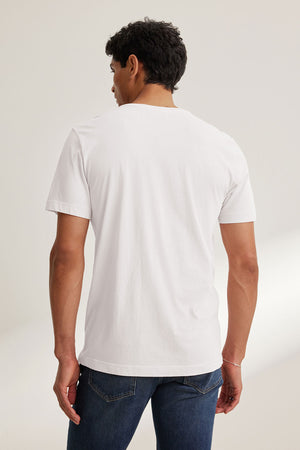 A man faces away from the camera, wearing the Velvet by Graham & Spencer HOWARD TEE, a plain white Pima jersey t-shirt, paired with blue jeans against a neutral background.