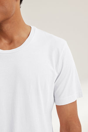A person is wearing the HOWARD TEE by Velvet by Graham & Spencer, a plain white t-shirt crafted from lightweight Pima jersey, set against a neutral background, highlighting the upper torso and part of the neck for an ideal fit with a vintage vibe.