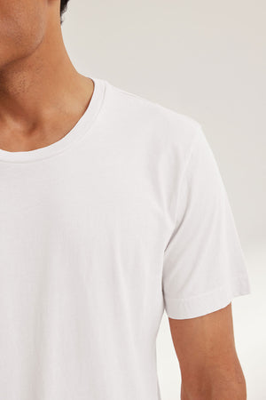 A person wears the HOWARD TEE by Velvet by Graham & Spencer, a plain white short-sleeve t-shirt with a perfect fit, shown from shoulders to upper chest against a neutral background.