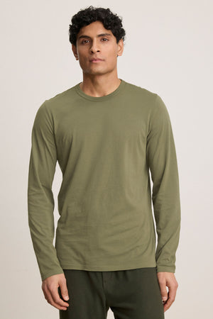 A person wears the Velvet by Graham & Spencer ROWLAND TEE in olive green with dark green pants, standing against a plain light background.