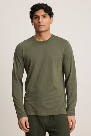 A person stands facing forward, wearing the ROWLAND TEE by Velvet by Graham & Spencer—an olive green long-sleeve crewneck—paired with matching pants against a plain background.