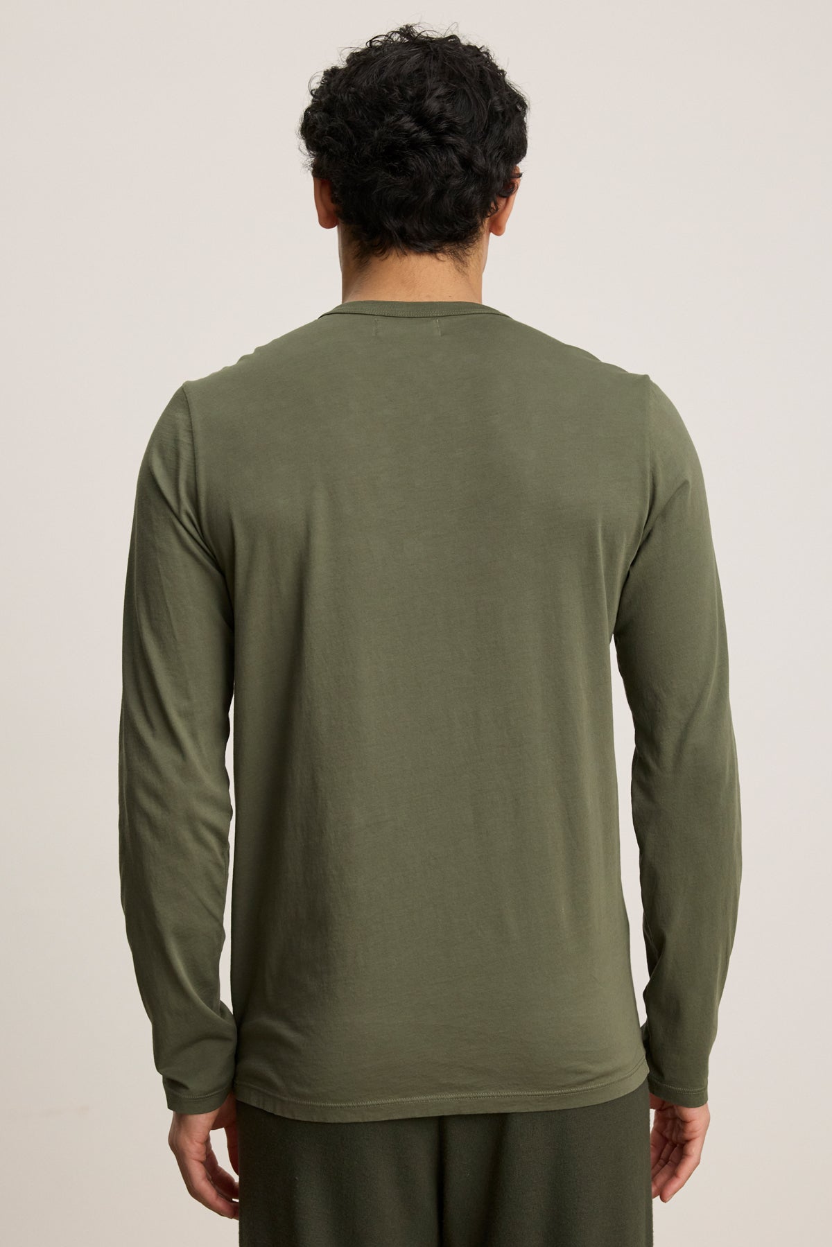 A person with short curly hair faces away from the camera, wearing the ROWLAND TEE by Velvet by Graham & Spencer in olive green, paired with matching pants, standing against a plain background.-40054349234369