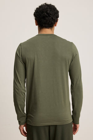 A person with short curly hair faces away from the camera, wearing the ROWLAND TEE by Velvet by Graham & Spencer in olive green, paired with matching pants, standing against a plain background.