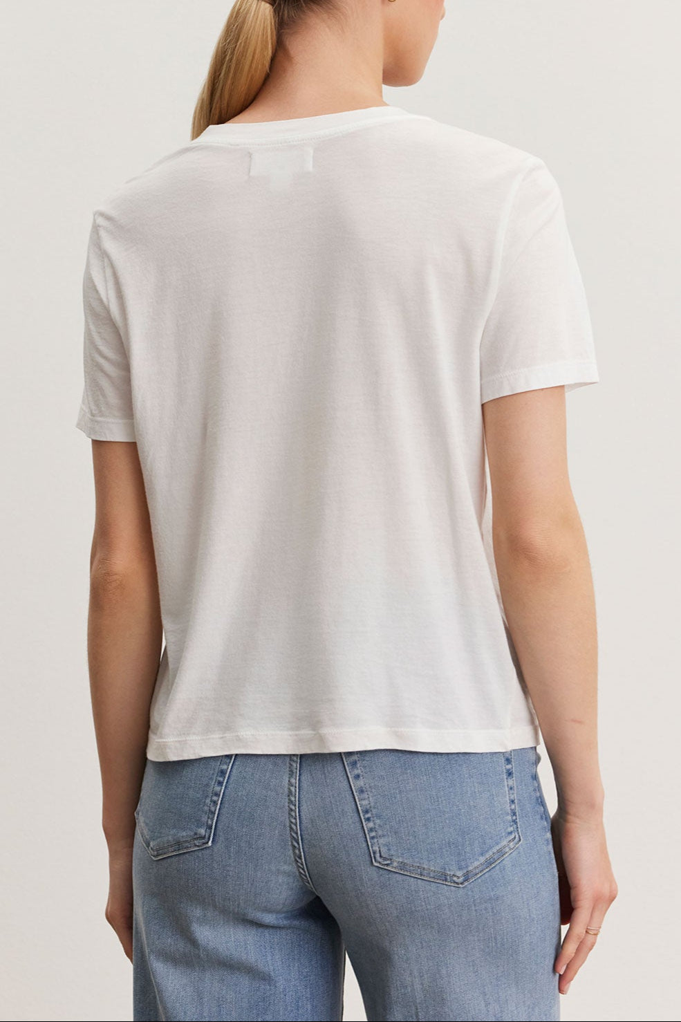 Rear view of a woman with a ponytail wearing a Velvet by Graham & Spencer RYAN TEE in whisper cotton fabric and blue jeans, standing against a light background.-36998721831105