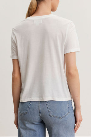 Rear view of a woman with a ponytail wearing a Velvet by Graham & Spencer RYAN TEE in whisper cotton fabric and blue jeans, standing against a light background.