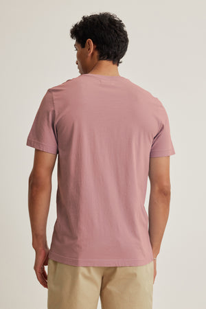 A person faces away, wearing the SAMSEN TEE by Velvet by Graham & Spencer—a light pink Pima jersey v-neck tee—paired with beige pants against a plain background, ideal for everyday wear.