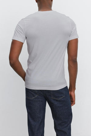 Man wearing a Velvet by Graham & Spencer SAMSEN TEE with a v-neckline and dark blue jeans, standing with his back to the camera against a plain white background.