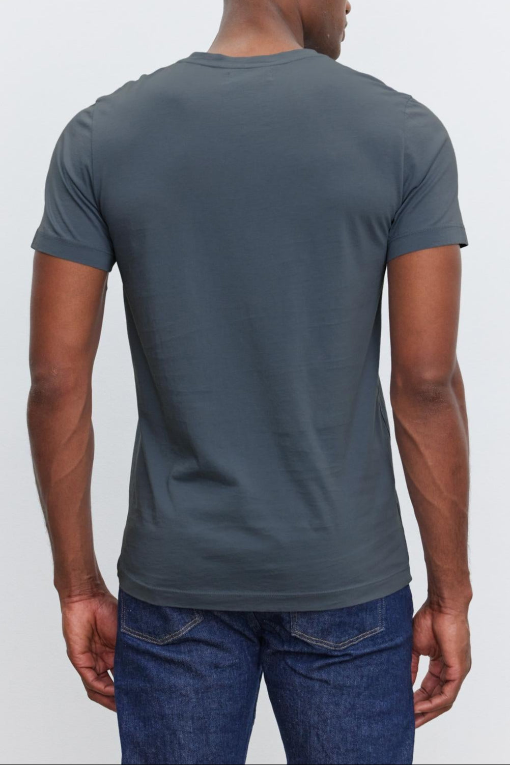 A person wearing a dark gray SAMSEN TEE by Velvet by Graham & Spencer and blue jeans is standing with their back to the camera.