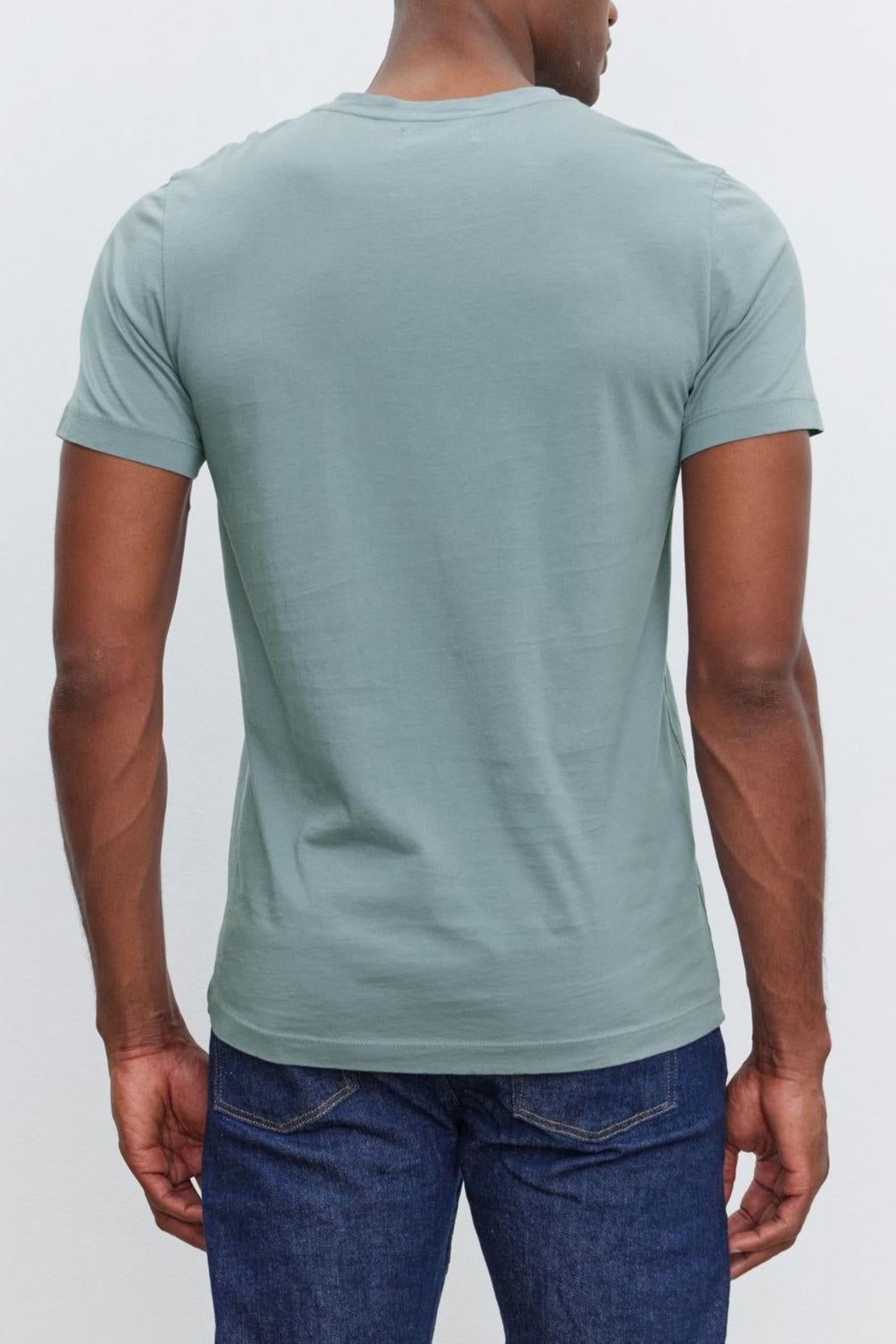 A person is standing with their back to the camera, wearing a light blue SAMSEN TEE by Velvet by Graham & Spencer and dark blue jeans against a plain white background.
