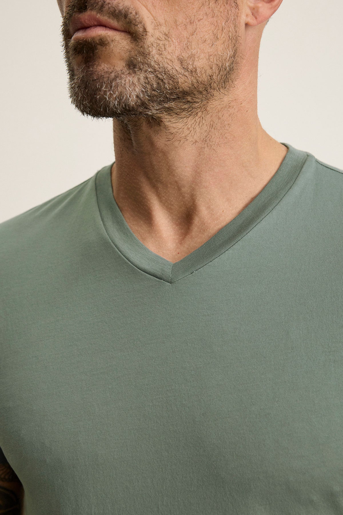 A man in a SAMSEN TEE from Velvet by Graham & Spencer, displays a green V-neck Pima jersey, highlighting the V-neckline and part of his bearded face, perfect for stylish layering.