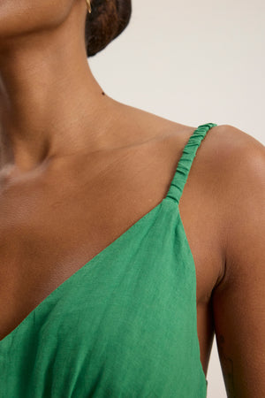 Close-up of a person wearing the JANET LINEN DRESS by Velvet by Graham & Spencer—a green woven linen tank dress with spaghetti straps—showing their shoulder, neck, and part of their upper chest.