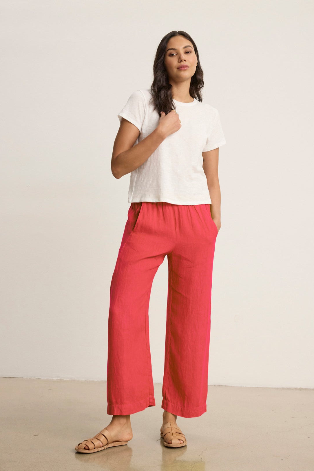 Someone wearing the LOLA LINEN PANT by Velvet by Graham & Spencer, styled with a white t-shirt, stands relaxed with one hand in their pocket against a plain background.-38812900196545
