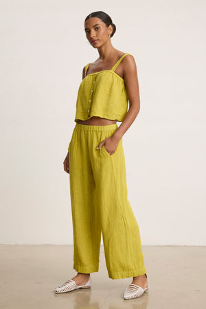 A woman poses in a studio wearing the Velvet by Graham & Spencer LOLA LINEN PANT—light green, pull-on linen trousers with a relaxed leg—paired with a matching sleeveless crop top and white woven shoes.