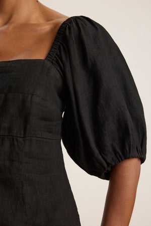 A person wearing the OLIVIA LINEN TOP by Velvet by Graham & Spencer—a black woven linen top with a square neckline and puff sleeves.