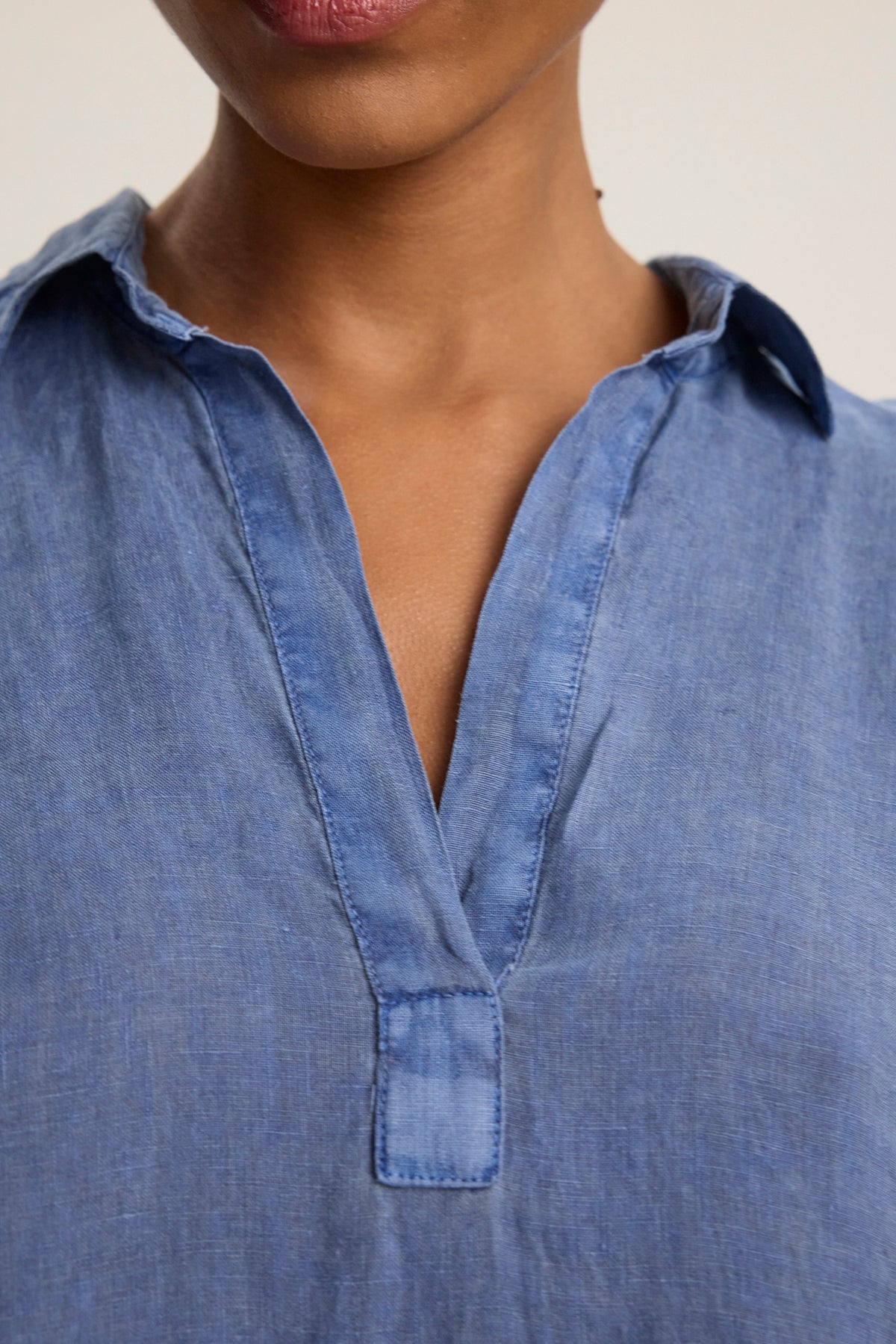 Close-up of a person wearing the STELLA LINEN DRESS by Velvet by Graham & Spencer, showcasing its blue collared V-neck design and versatile silhouette that complements any look. Lower half of face and neck visible.-39123406586049