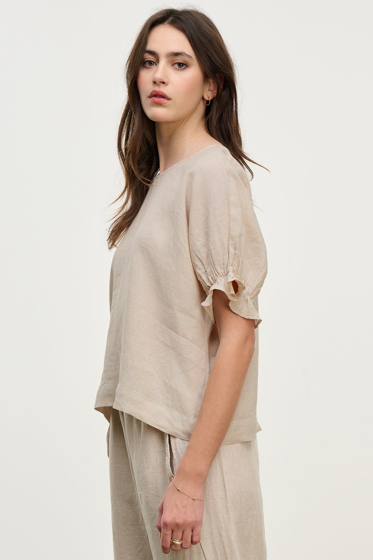 A woman with long brown hair in a Velvet by Graham & Spencer EMILY LINEN TOP, featuring ruffle cuffs and a boxy fit, gazes neutrally at the camera against a plain, light background.-38662581715137