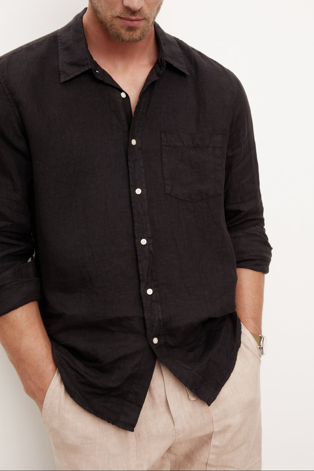 A stylish man in a Velvet by Graham & Spencer BENTON LINEN BUTTON-UP SHIRT leaning against a wall.-36009360425153