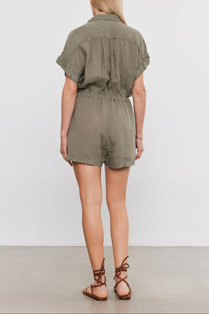 Woman standing facing away, wearing an olive green Velvet by Graham & Spencer CLARE LINEN ROMPER with drawstring waist and brown lace-up sandals.