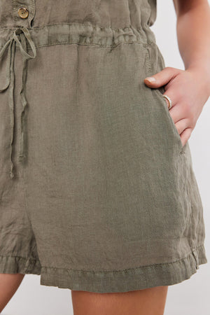 Close-up of a person wearing a Velvet by Graham & Spencer CLARE LINEN ROMPER with their hand lightly touching the breathable fabric.