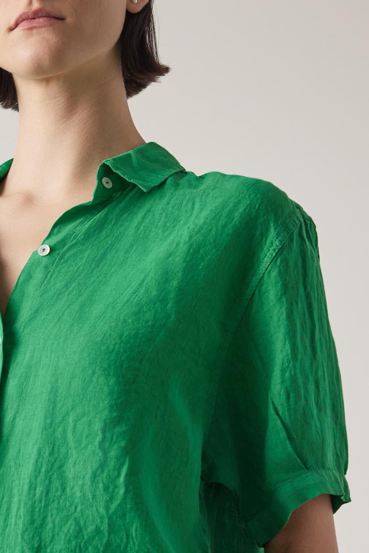   Close-up of a woman in a Velvet by Jenny Graham CLAREMONT LINEN SHIRT in bright green, focusing on the collar and upper part of the shirt, with a neutral background. 