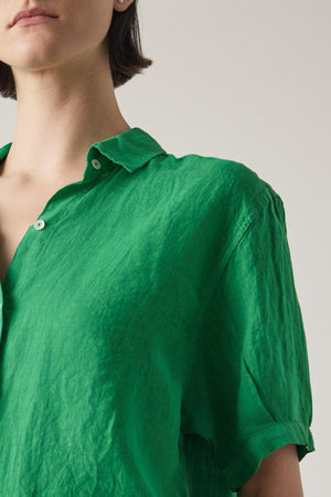 Close-up of a woman in a Velvet by Jenny Graham CLAREMONT LINEN SHIRT in bright green, focusing on the collar and upper part of the shirt, with a neutral background.