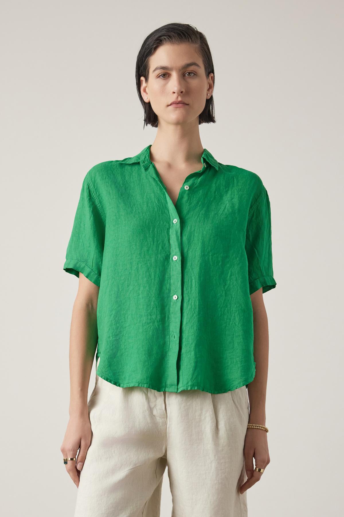   A person with short hair wearing a Velvet by Jenny Graham CLAREMONT LINEN SHIRT in bright green, and cream pants, standing against a light background. 