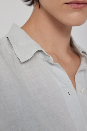 Close-up of a person wearing a Velvet by Jenny Graham Claremont Linen Shirt, focusing on the collar and top button, with part of their lower face visible.