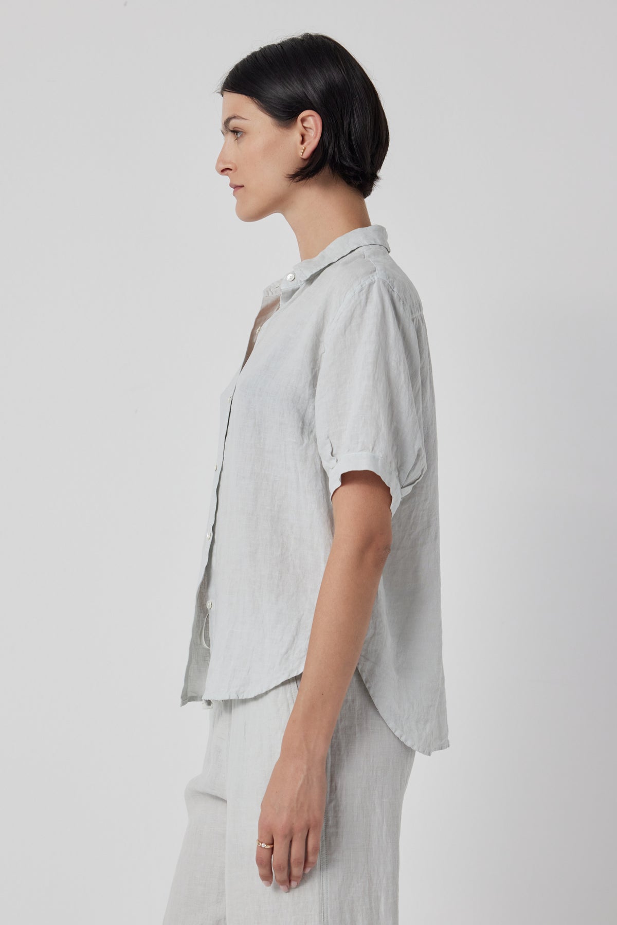 Profile view of a woman with short black hair wearing a Velvet by Jenny Graham Claremont Linen Shirt in light gray, standing against a plain background.-36168678342849