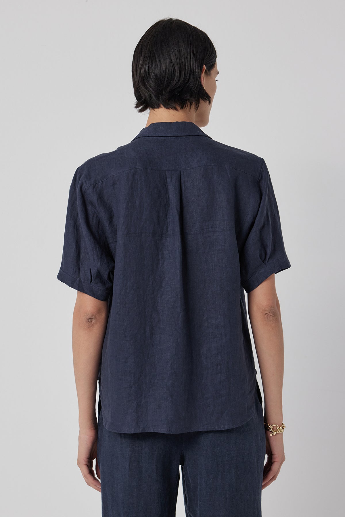 Rear view of a person with shoulder-length black hair, wearing a CLAREMONT LINEN SHIRT by Velvet by Jenny Graham and matching pants, standing against a light gray background.-36409572720833