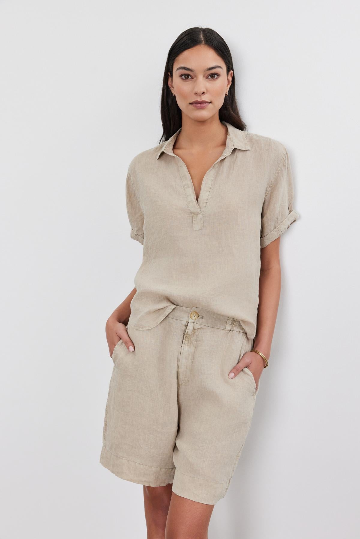A woman stands against a white background, wearing a Velvet by Graham & Spencer ELERIE LINEN TOP with a split neck collar and matching shorts, with her hands in her pockets.-36910008533185