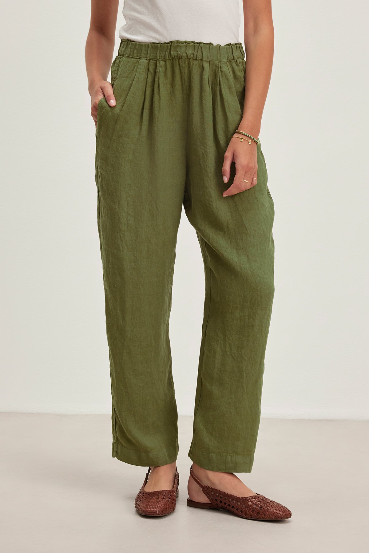 Wearing Velvet by Graham & Spencer's GINI LINEN PANT with an elastic waistband and straight-leg silhouette, paired with brown woven flats, a person stands relaxed with one hand in their pocket and a bracelet on one wrist, crafting a breezy look perfect for casual outings.-38662677233857