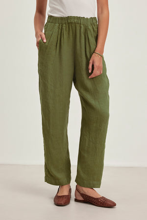 Wearing Velvet by Graham & Spencer's GINI LINEN PANT with an elastic waistband and straight-leg silhouette, paired with brown woven flats, a person stands relaxed with one hand in their pocket and a bracelet on one wrist, crafting a breezy look perfect for casual outings.
