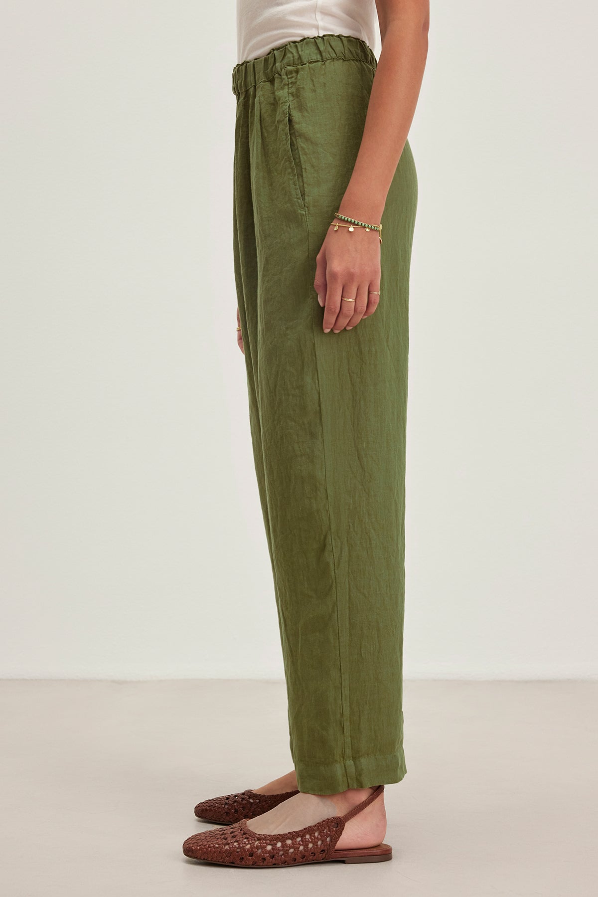 A person in a white top and Velvet by Graham & Spencer's GINI LINEN PANT, featuring a green high-waisted straight-leg design, stands sideways showcasing brown woven shoes.-38662677266625