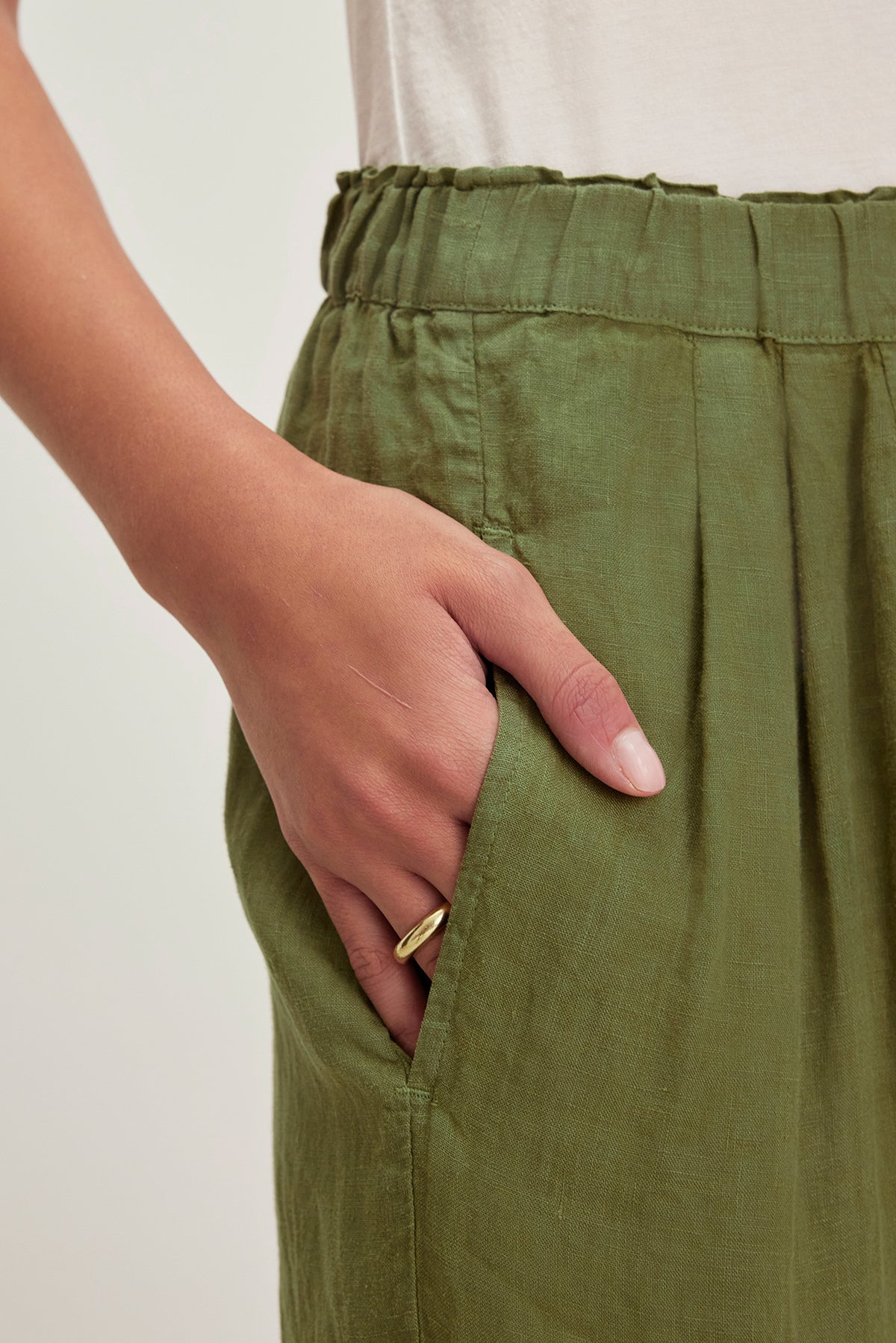 A hand wearing a ring is tucked into the pocket of a GINI LINEN PANT by Velvet by Graham & Spencer, featuring a straight-leg silhouette enhanced by lightweight woven linen.-38662677332161