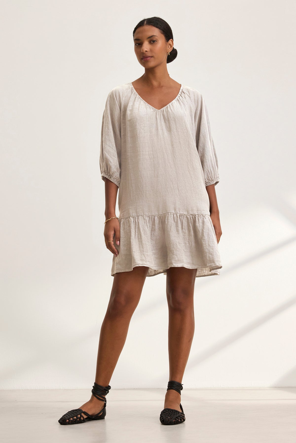 A woman models the Velvet by Graham & Spencer KAYLIE LINEN DRESS, featuring a loose fit, v-neck, and three-quarter sleeves. She pairs it with black ankle-strap flat shoes against a simple light background.-38943210635457