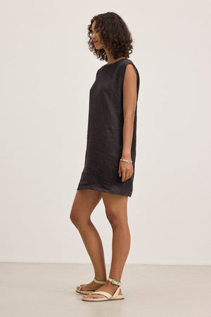 Person wearing the LARA LINEN DRESS by Velvet by Graham & Spencer, a sleeveless black dress, paired with sandals, standing against a plain white background.