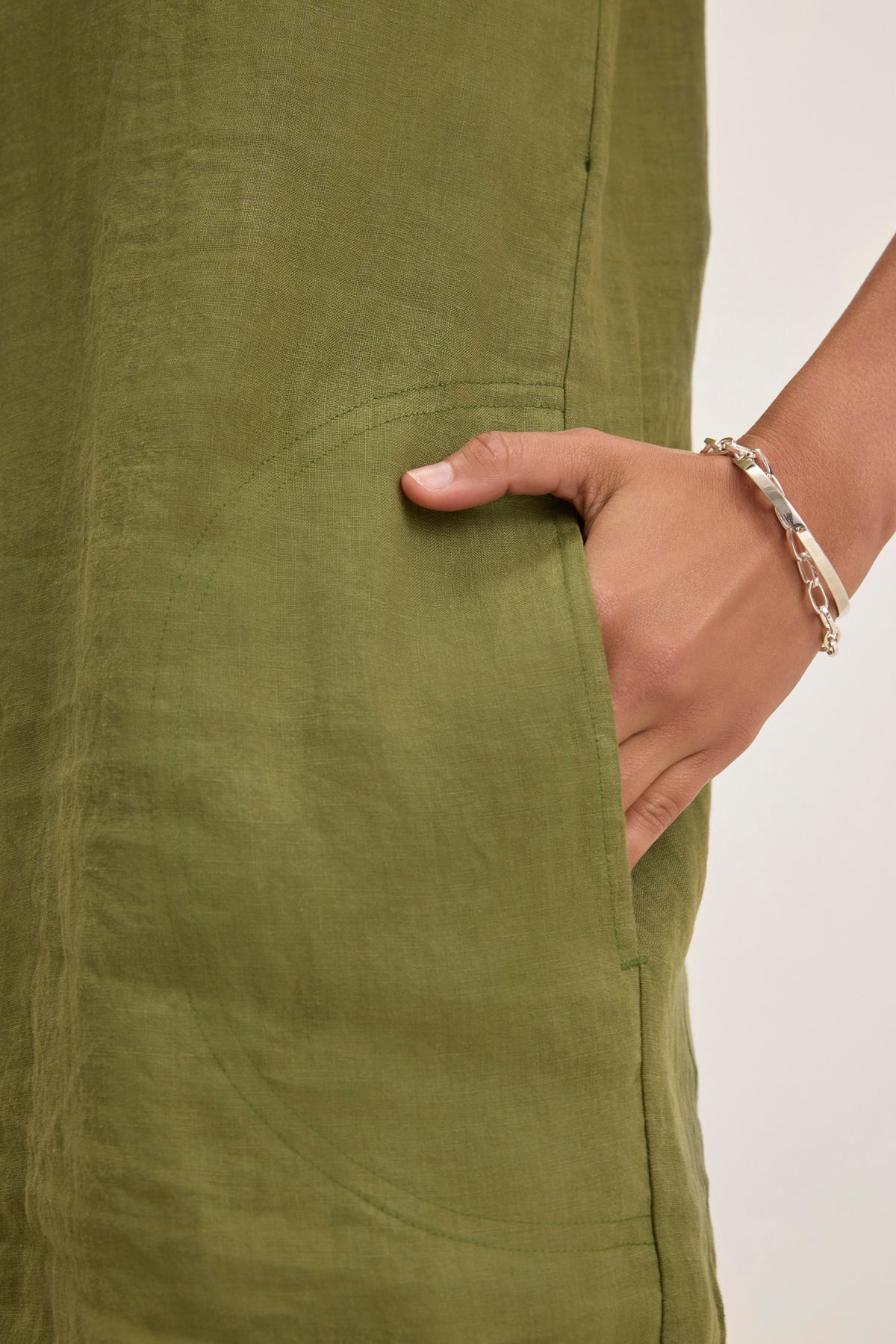 A hand with a bracelet is placed in the pocket of a LARA LINEN DRESS by Velvet by Graham & Spencer.