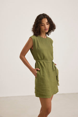A person wearing the sleeveless, knee-length LARA LINEN DRESS by Velvet by Graham & Spencer, complete with a belt, stands against a plain background.