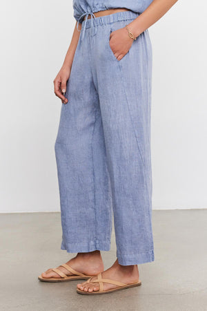 A person wearing Velvet by Graham & Spencer LOLA LINEN PANTS with an elastic waist and tan sandals, focusing on the lower half of the body.