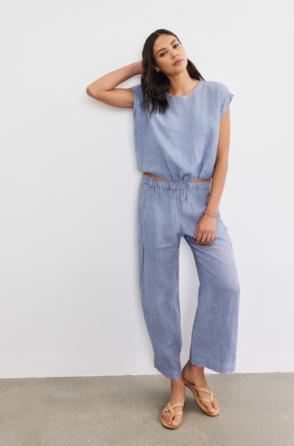 Woman in blue Velvet by Graham & Spencer LOLA LINEN PANT trousers leaning against a white wall, looking at the camera.-36910133149889