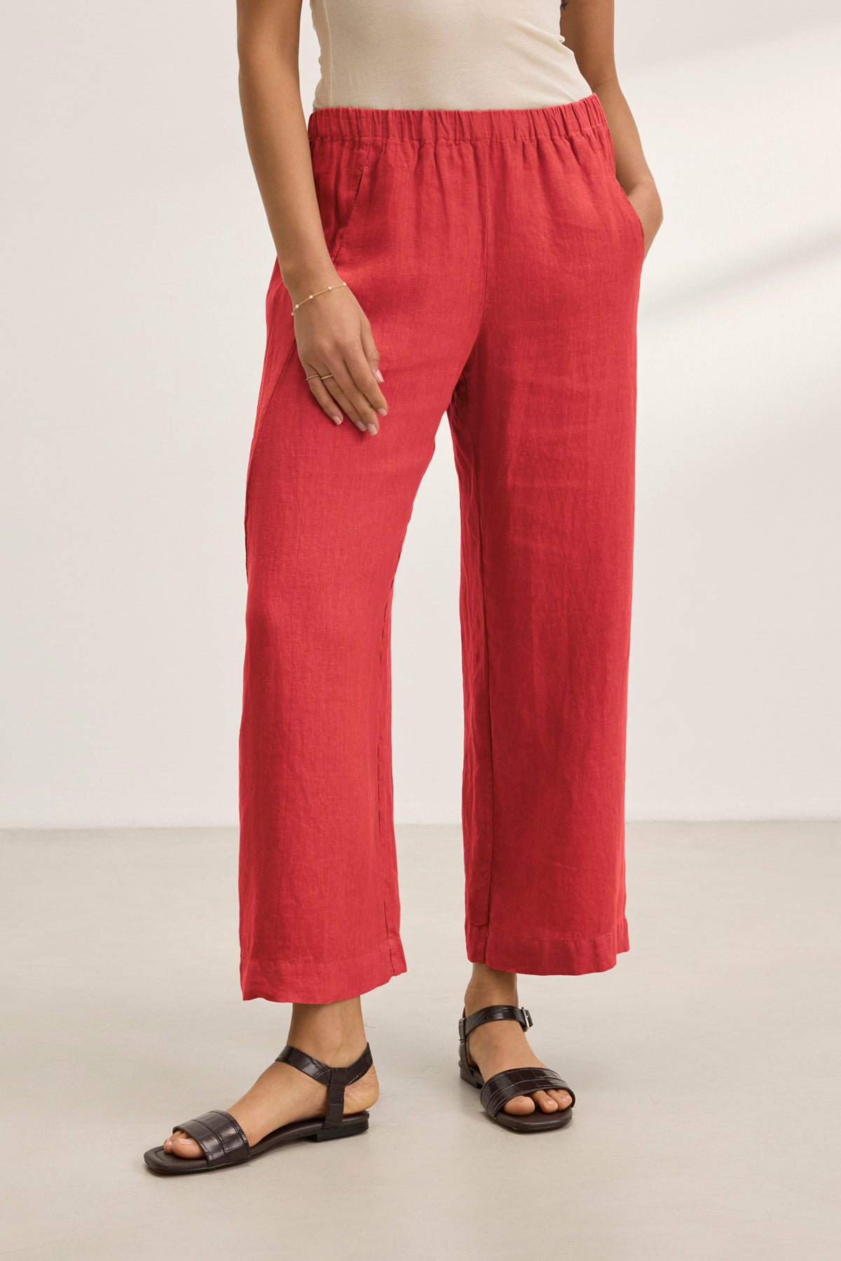 A person is indoors on a light floor, wearing Velvet by Graham & Spencer's stylish LOLA LINEN PANT in red with an elastic waist and paired with black sandals. Only the lower body is visible.-38812900032705