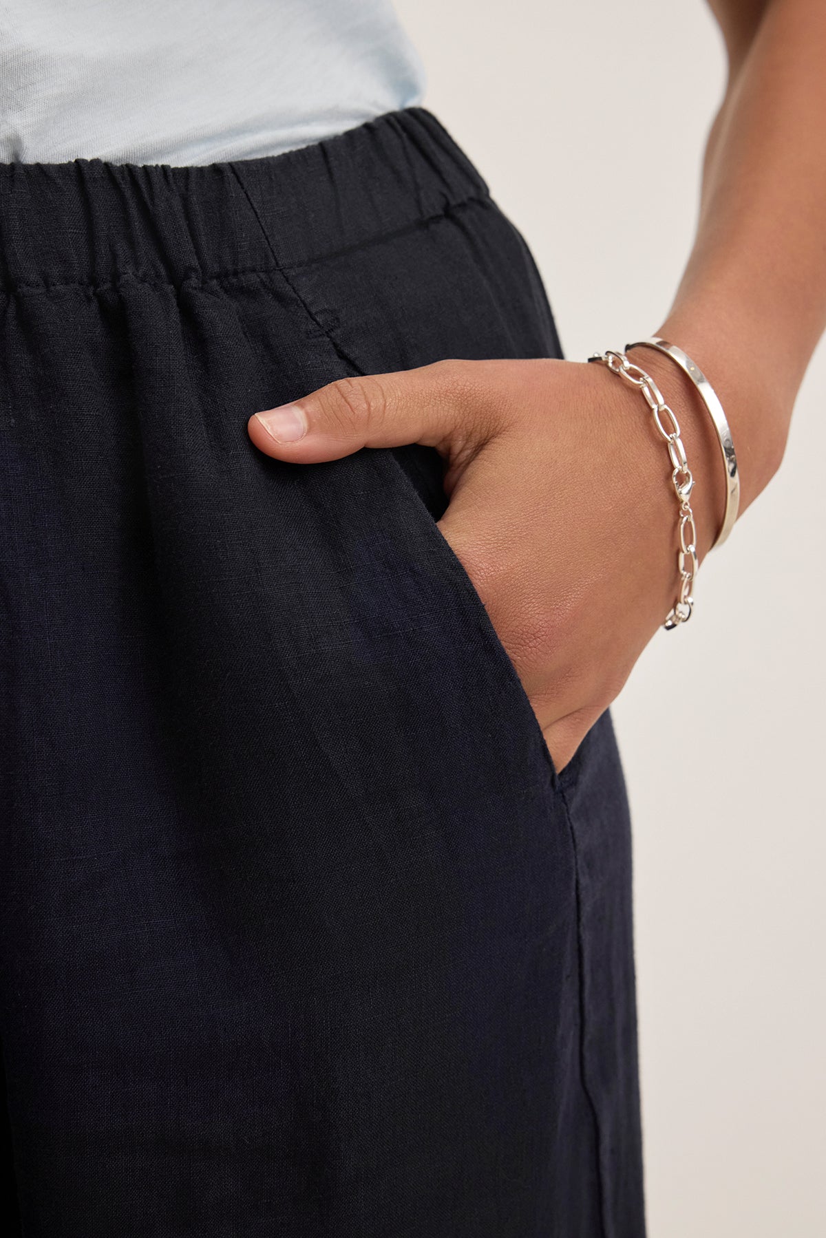 A person wearing LOLA LINEN PANT by Velvet by Graham & Spencer, featuring an elastic waist and a hand in the pocket, while sporting two silver bracelets.-38662705643713