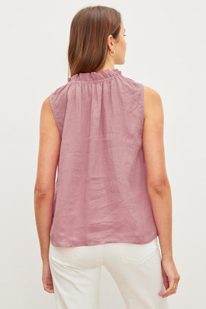 Woman standing with her back to the camera, wearing a Pink MASIE LINEN TANK TOP and white pants, against a plain background.