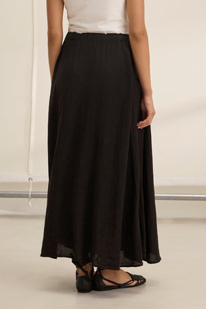 A person shown from the back wears a white sleeveless top, black flat sandals, and the MEMPHIS LINEN SKIRT by Velvet by Graham & Spencer—a long black linen maxi skirt with an elastic waist.