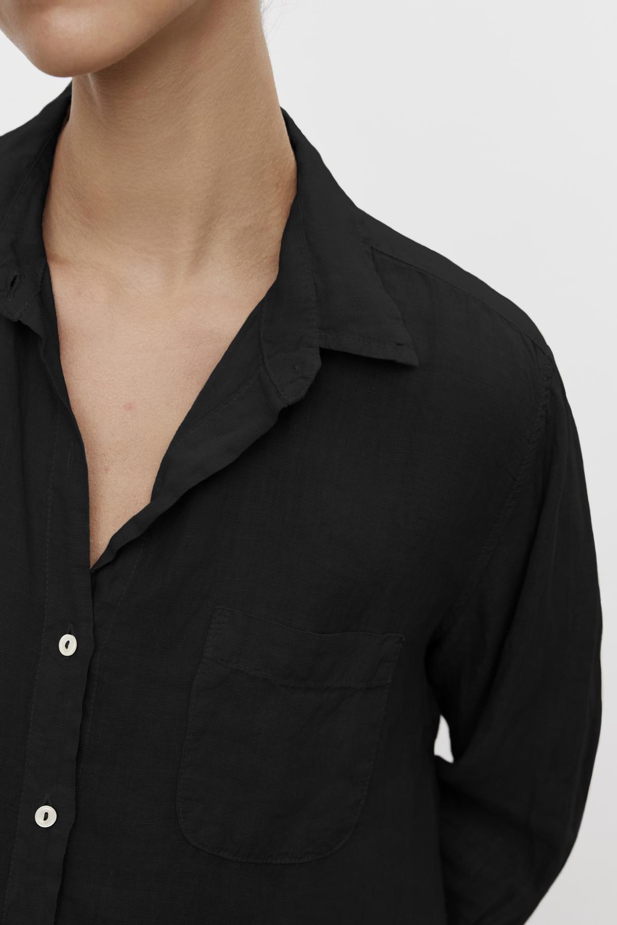 Close-up of a person wearing a Velvet by Jenny Graham MULHOLLAND LINEN SHIRT with a front pocket and an open collar. The shirt's fabric appears lightweight and textured, featuring a relaxed silhouette. The background is plain and light-colored.-36463599550657
