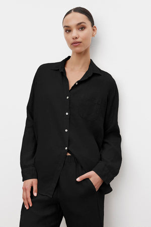 Woman wearing a black MULHOLLAND LINEN SHIRT by Velvet by Jenny Graham and black pants, standing against a plain white background with one hand in pocket.