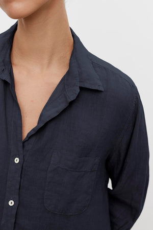 Close-up of a person wearing the MULHOLLAND LINEN SHIRT by Velvet by Jenny Graham, a dark blue linen button-up shirt with a left chest pocket. The shirt collar is slightly open, the sleeves are long, and it features a relaxed silhouette.